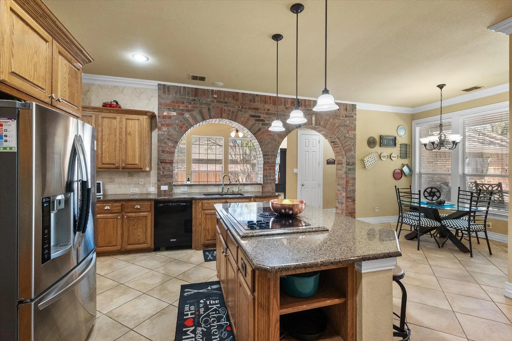Spacious **gourmet kitchen with center island** offers abundant prep space and functionality, perfect for everyday living and entertaining. Featuring **granite countertops, tile flooring, and sleek black appliances**, this kitchen is designed for both style and durability. Unique **brick wall accents with arched openings** add character and architectural charm, creating a warm and inviting atmosphere. With **extensive cabinetry, ample counter space, and an open layout**, this kitchen provides the ideal workspace for cooking, gathering, and hosting.