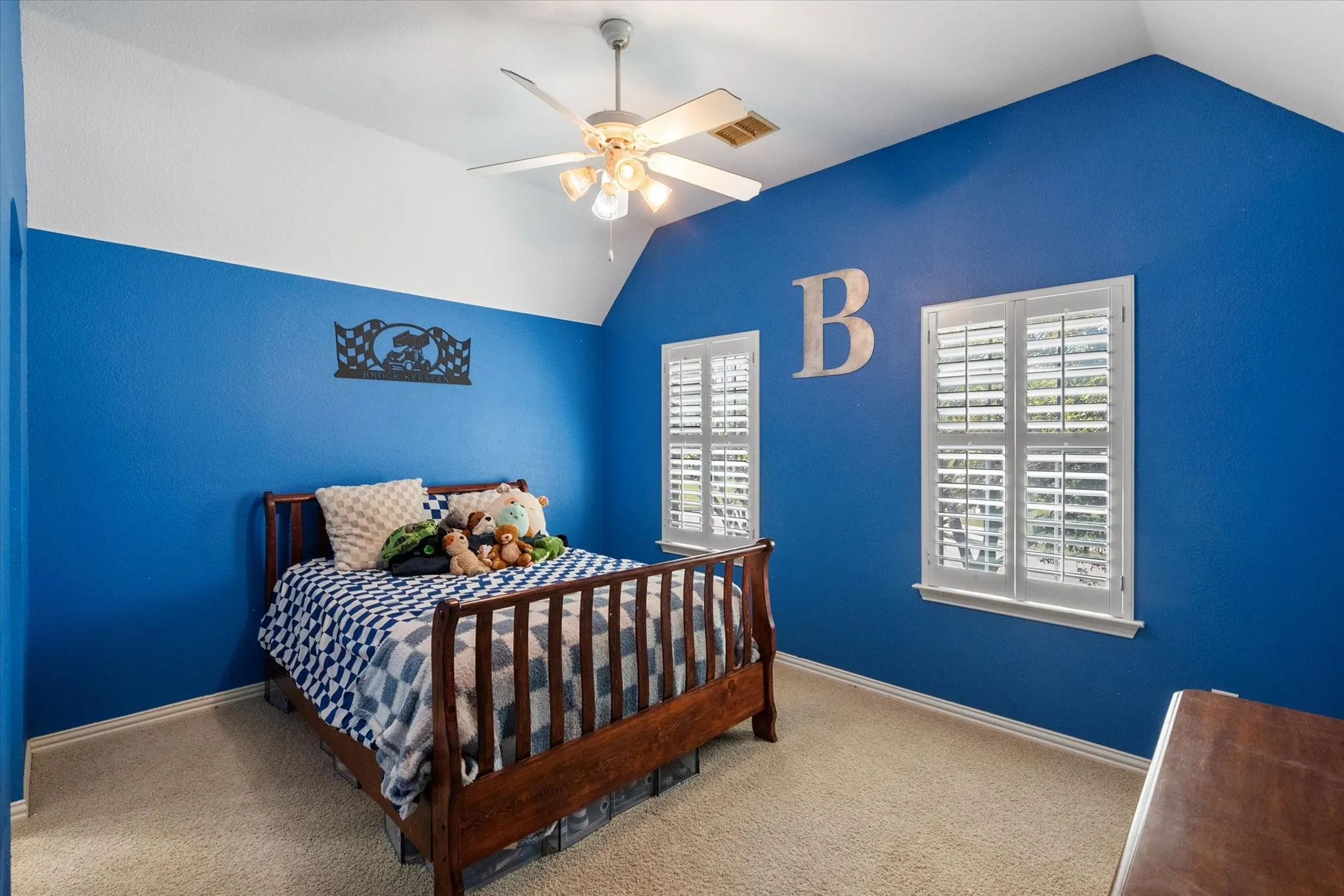 Bright and spacious upstairs secondary bedroom featuring a wall of windows that fills the room with natural light. Vaulted ceiling adds an open, airy feel, while plantation shutters provide both style and privacy. Comfortable layout includes plush carpeting, a ceiling fan, and a generously sized closet for ample storage. Ideal space for a bedroom, guest room, or home office with a perfect blend of function and charm.