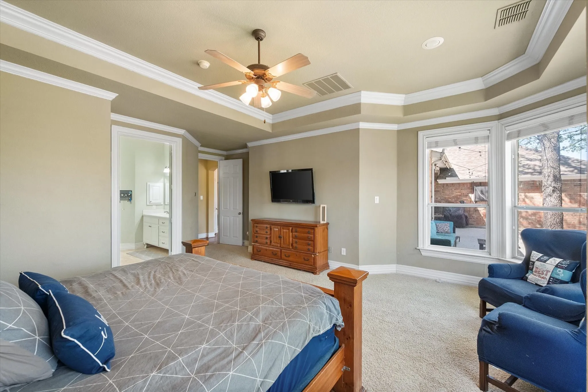 Spacious primary bedroom featuring elegant tray ceilings accented with crown molding and recessed can lighting, creating a refined and inviting atmosphere. Generously sized to accommodate a king-size bed and a comfortable sitting area, this private retreat offers both functionality and style. Plush carpeting enhances comfort, while abundant natural light and thoughtful layout provide a relaxing space perfect for unwinding at the end of the day.