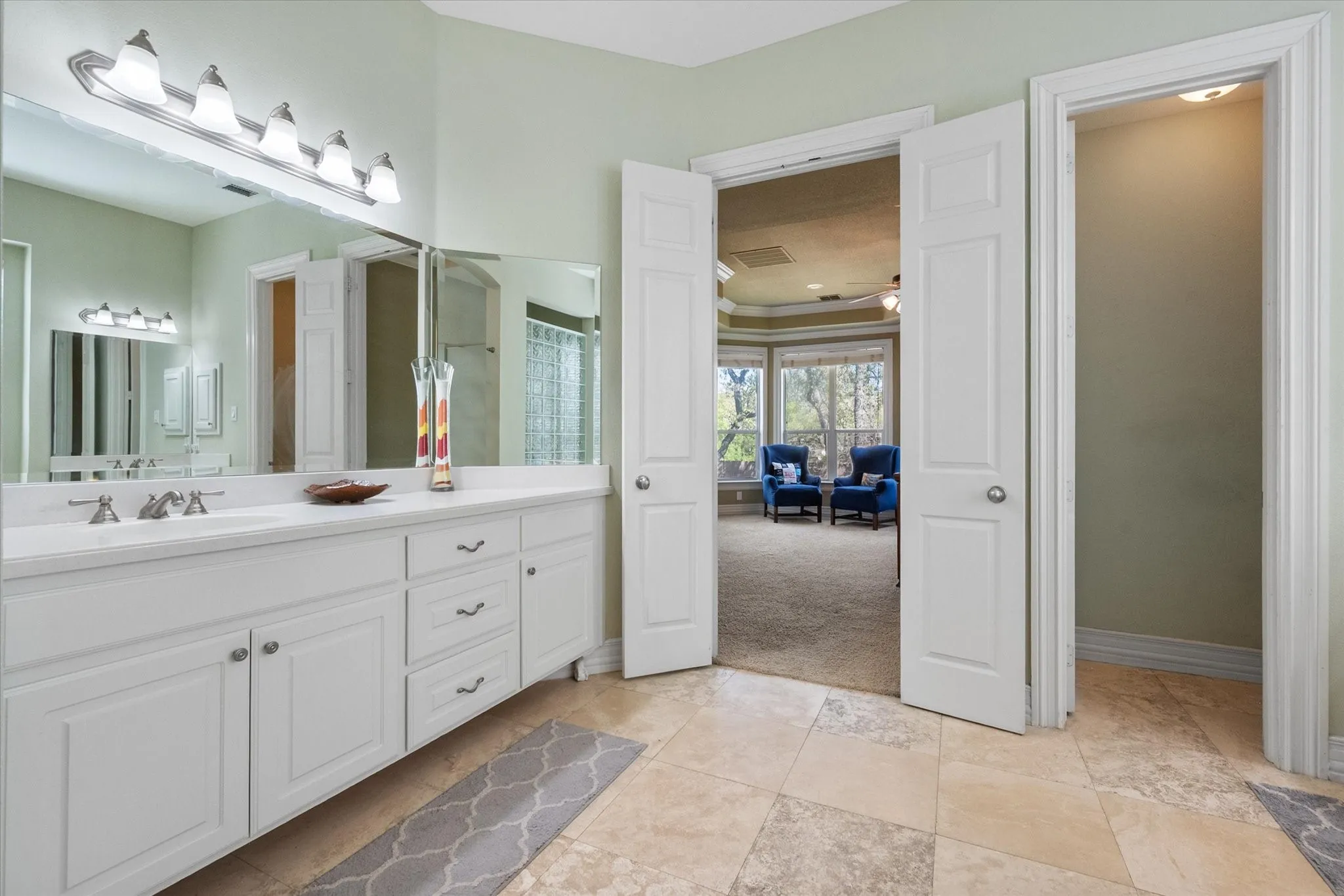 Spa-like primary bathroom retreat featuring dual vanities with abundant counter space, ideal for everyday convenience and getting ready with ease. Elegant travertine tile flooring adds warmth and durability, while oversized mirrors and bright vanity lighting provide excellent illumination. Thoughtfully designed layout offers privacy and functionality, creating a comfortable and relaxing space that complements the primary suite.