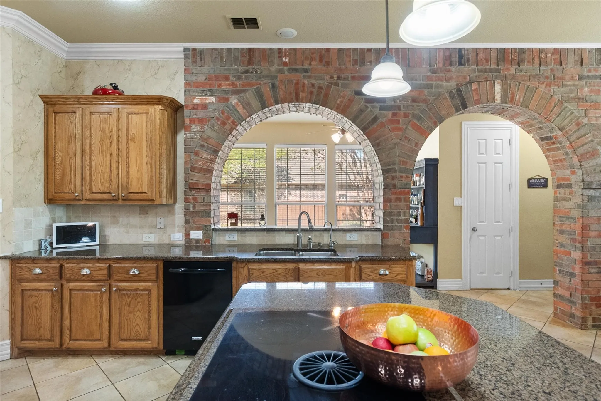 Close up photo of center island cooktop with 5 burners. This kitchen is a cook's dream. The custom cabinets offer abundant storage. The brick wall features give a bit of flair to the room.