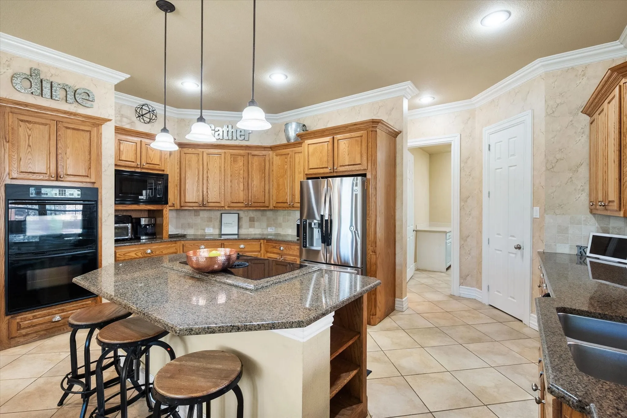Expansive **chef’s kitchen with oversized center island and breakfast bar**, perfect for casual dining and entertaining. This beautifully designed space features **granite countertops, custom wood cabinetry, and sleek black appliances**, offering both style and functionality. The **large island provides ample seating and prep space**, while **pendant lighting adds a warm, inviting ambiance**. Enjoy abundant storage, generous counter space, and an efficient layout ideal for everyday living. Designed for gatherings, this **open-concept kitchen** seamlessly connects to surrounding living areas, making it the heart of the home.
