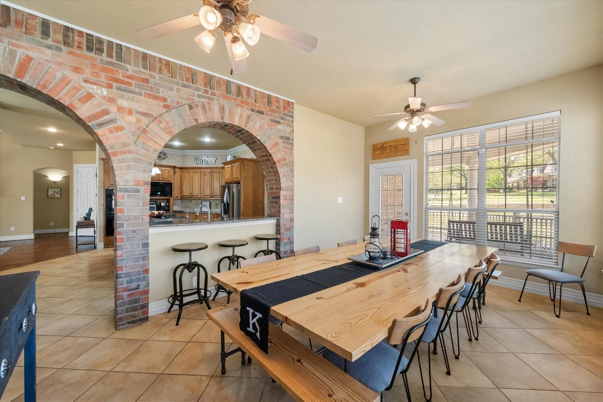 Bright and versatile sunroom seamlessly connected to the kitchen through stunning brick archways, creating an open-concept feel ideal for entertaining. This flexible space can serve as a spacious dining area, secondary living room, or cozy sitting area. Features include tile flooring, abundant natural light, ceiling fans, and a convenient door leading to the side porch for easy indoor-outdoor living. Perfect for relaxing, hosting, or creating a multi-functional living space to fit your lifestyle.