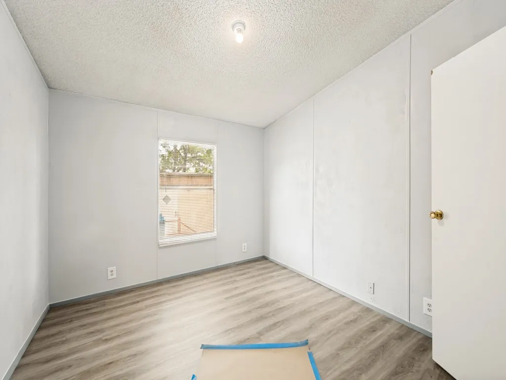 Room featuring light gray wall paneling, wood-finish flooring, a single window, and a ceiling-mounted light fixture