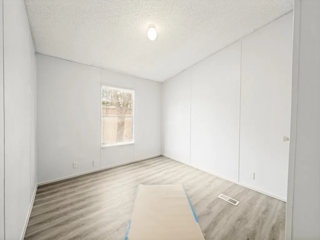 Bright interior space featuring a window, wood-finish flooring, white walls, and a textured ceiling