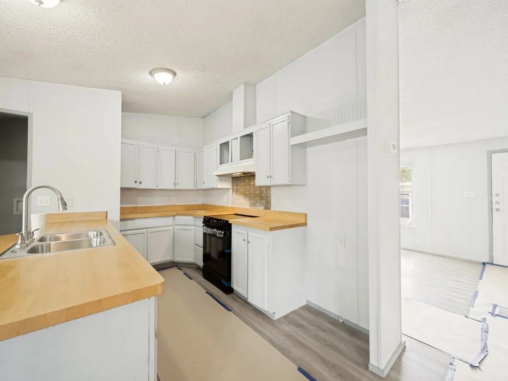 U-shaped kitchen featuring white cabinetry, wood-finish countertops, and a stainless steel double sink with a gooseneck faucet