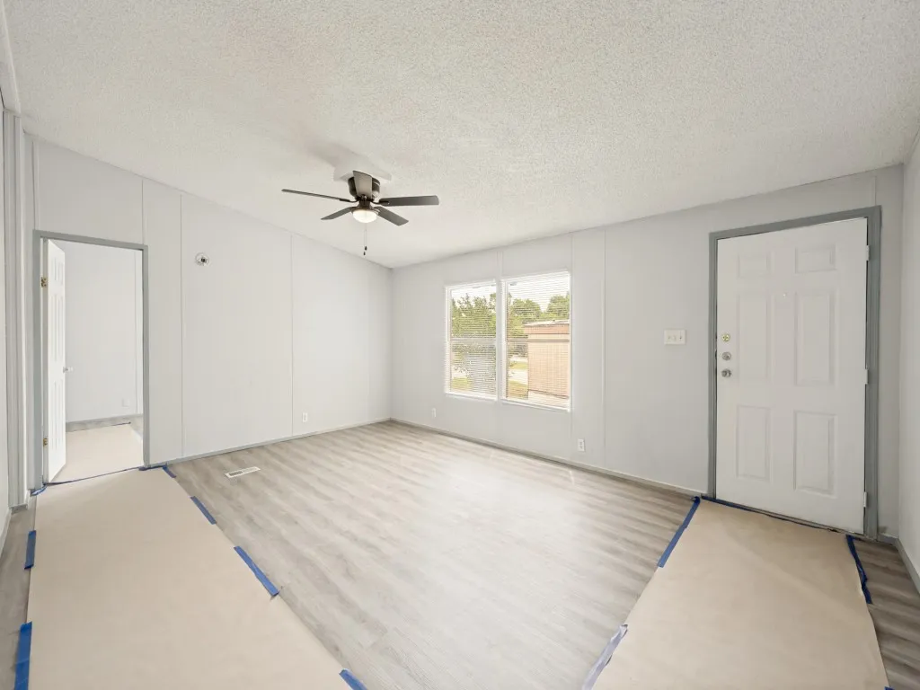 Spacious room featuring wood-finish flooring, light grey walls, a multi-pane window, and a ceiling fan with integrated lighting