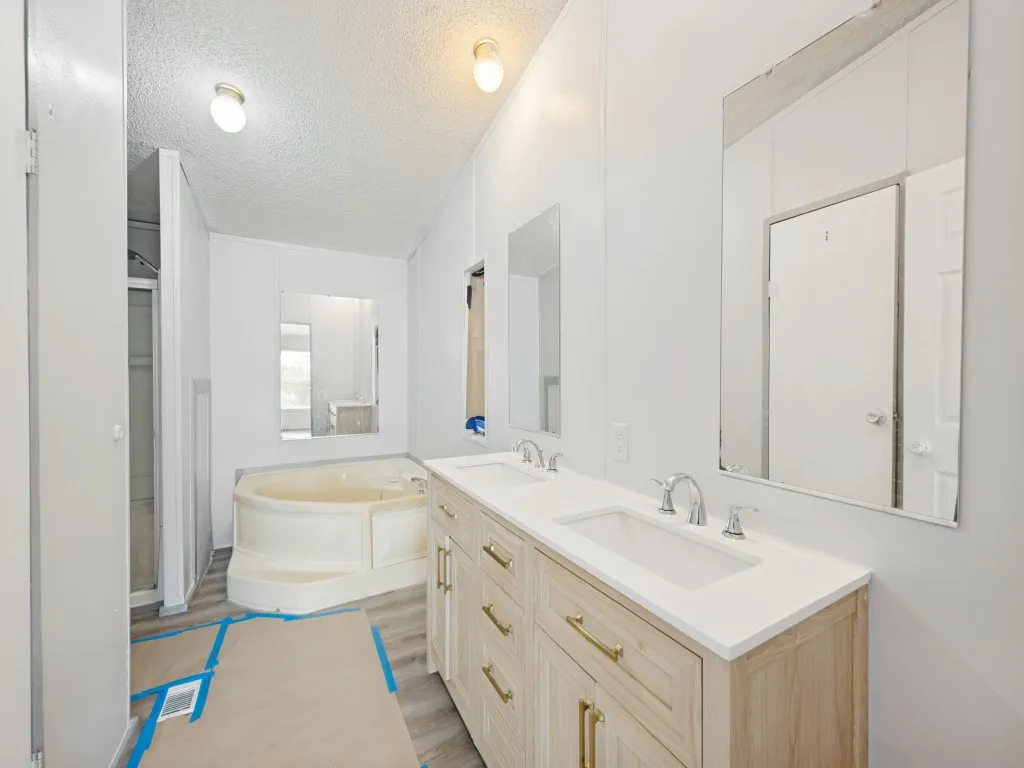 Bathroom featuring a double vanity with light wood cabinetry, white countertops, and chrome fixtures