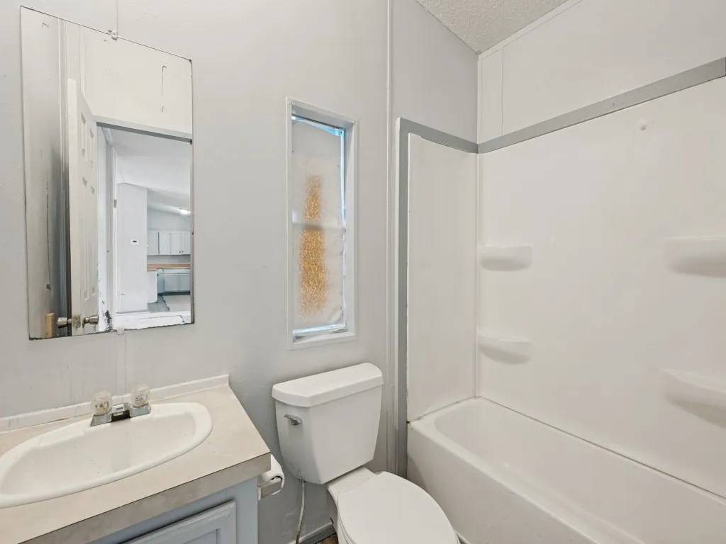 Bathroom featuring a white bathtub with integrated shelving, a white toilet, and a vanity with an integrated sink and light-colored countertop