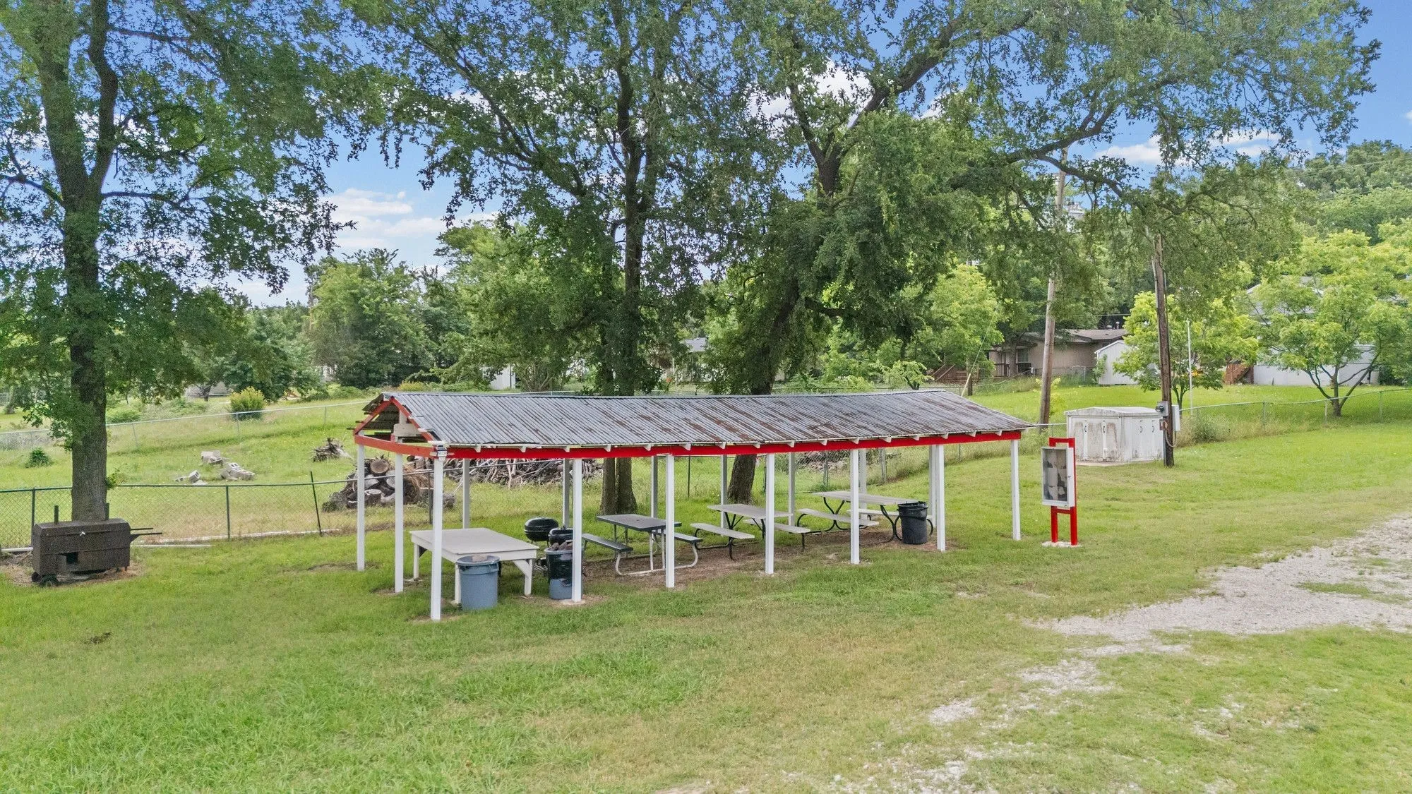 Expansive outdoor covered area featuring a red and white metal roof structure, supported by white posts, set on a manicured lawn at HOA Park.