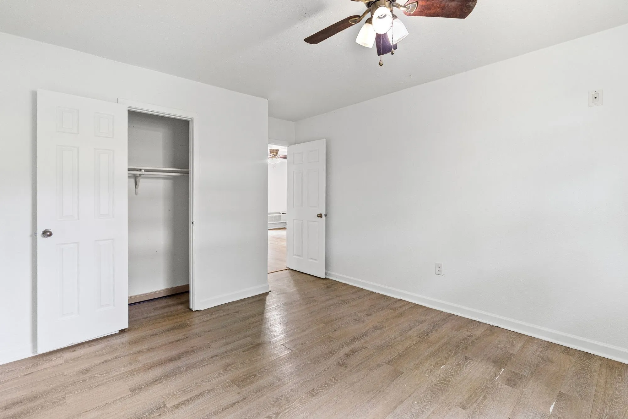 Interior room featuring light wood-finish flooring, white walls, and a ceiling fan with integrated lighting