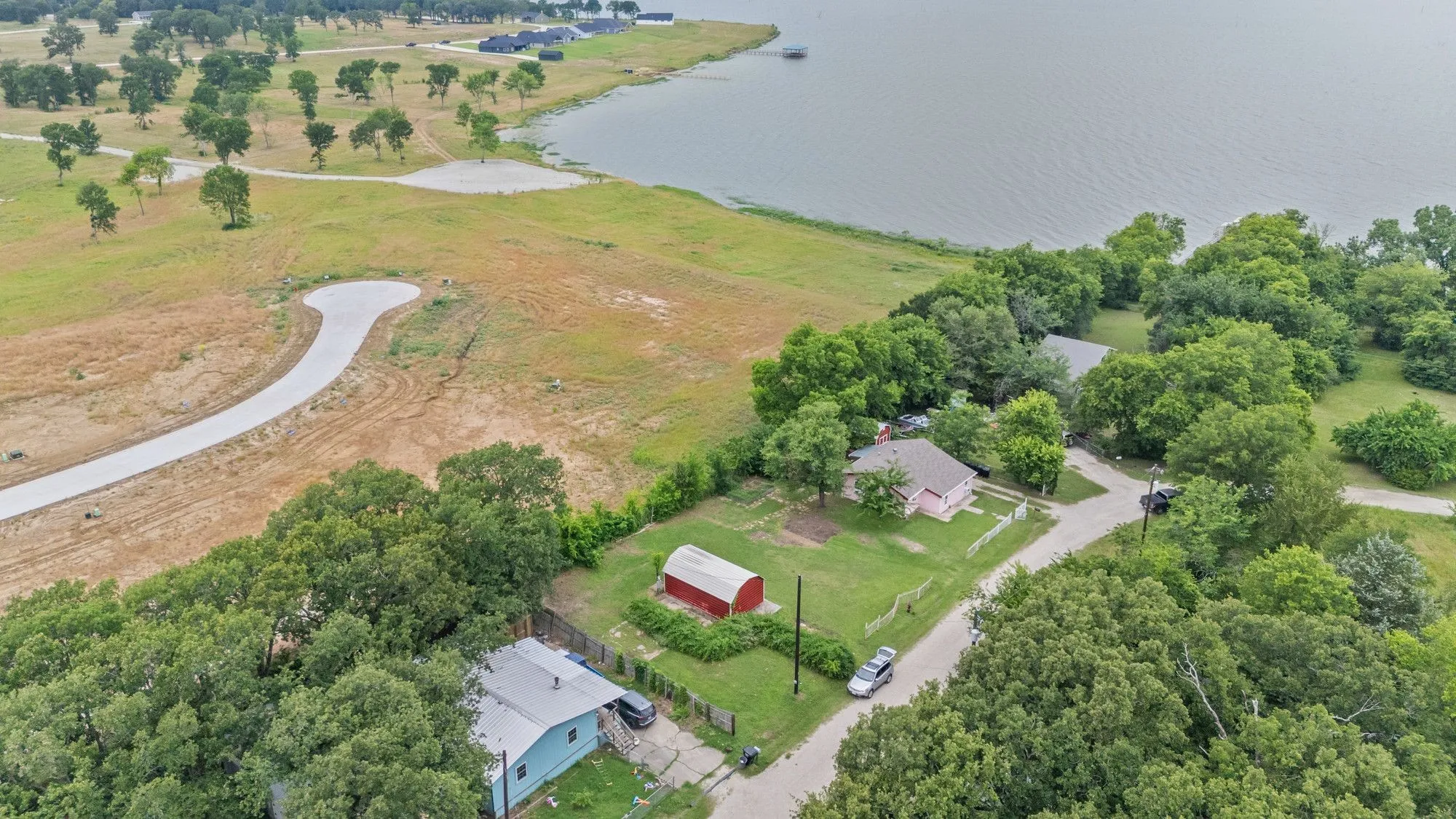 Aerial perspective showcasing water frontage, surrounding green spaces, and a newly paved cul-de-sac