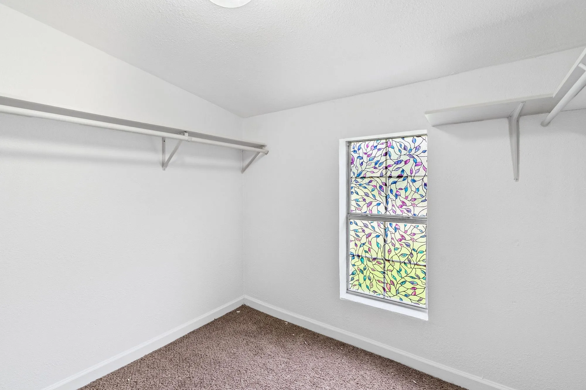 Carpeted room featuring a decorative window, white walls, and built-in closet shelving