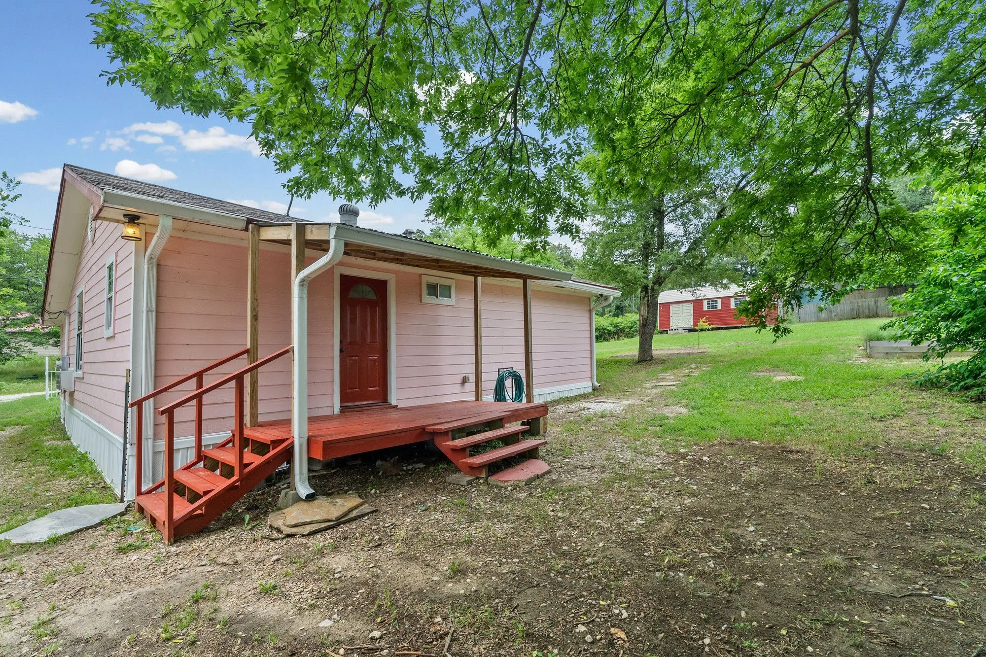 Pink-sided residence featuring a red entry door, a covered porch with red steps, and a white gutter system