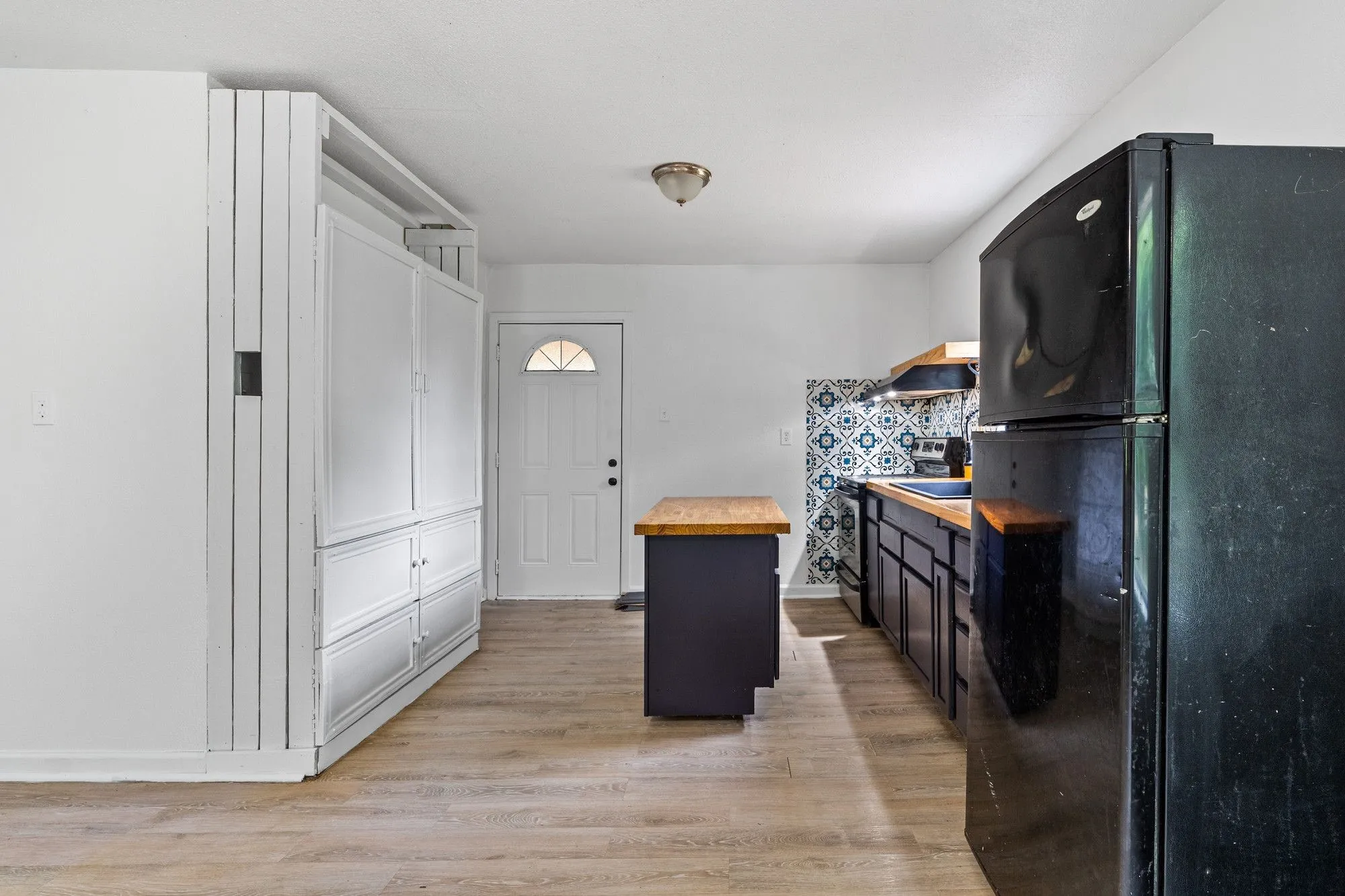 Kitchen featuring wood-finish flooring, a patterned tile backsplash, dark cabinetry, and wood countertops