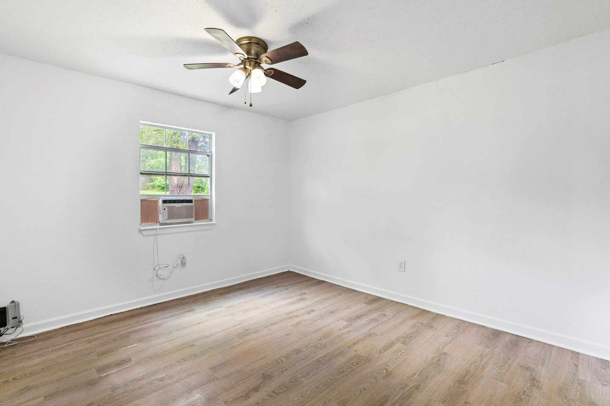 Room featuring wood-finish flooring, white walls, and a window with a window-mounted air conditioning unit