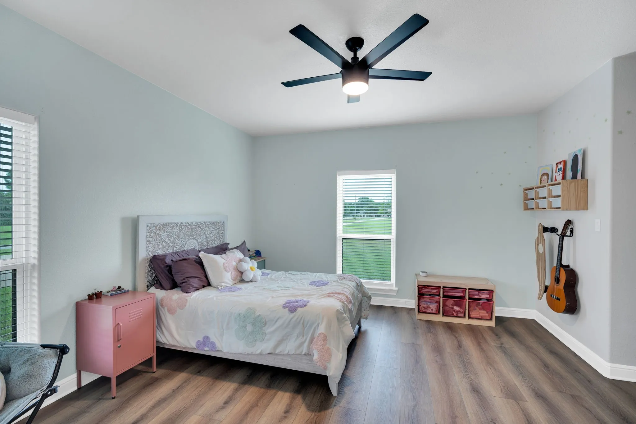 Bedroom 3 featuring a sitting nook with upper builtin cabinetry, a personal bathroom vanity, a modern ceiling fan with integrated lighting, and two windows with views of the front and side yard.