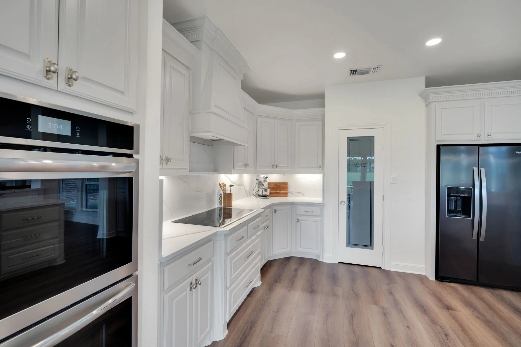 Modern kitchen featuring white cabinetry, integrated stainless steel appliances, and a large pantry with custom cabinetry.