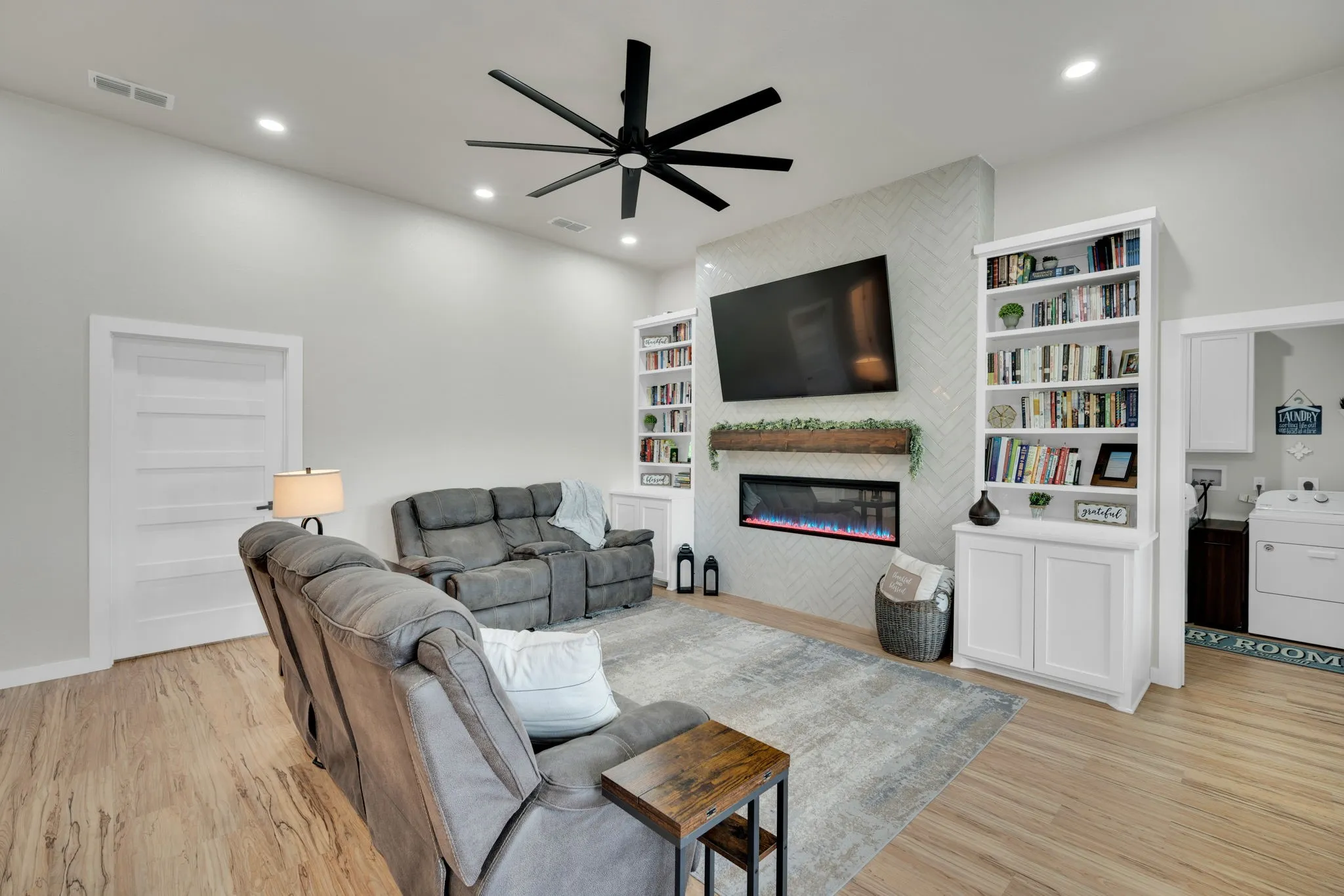 Spacious living area featuring a large tile electric fireplace, built in cabinetry with book shelves, recessed lighting, and a contemporary ceiling fan.