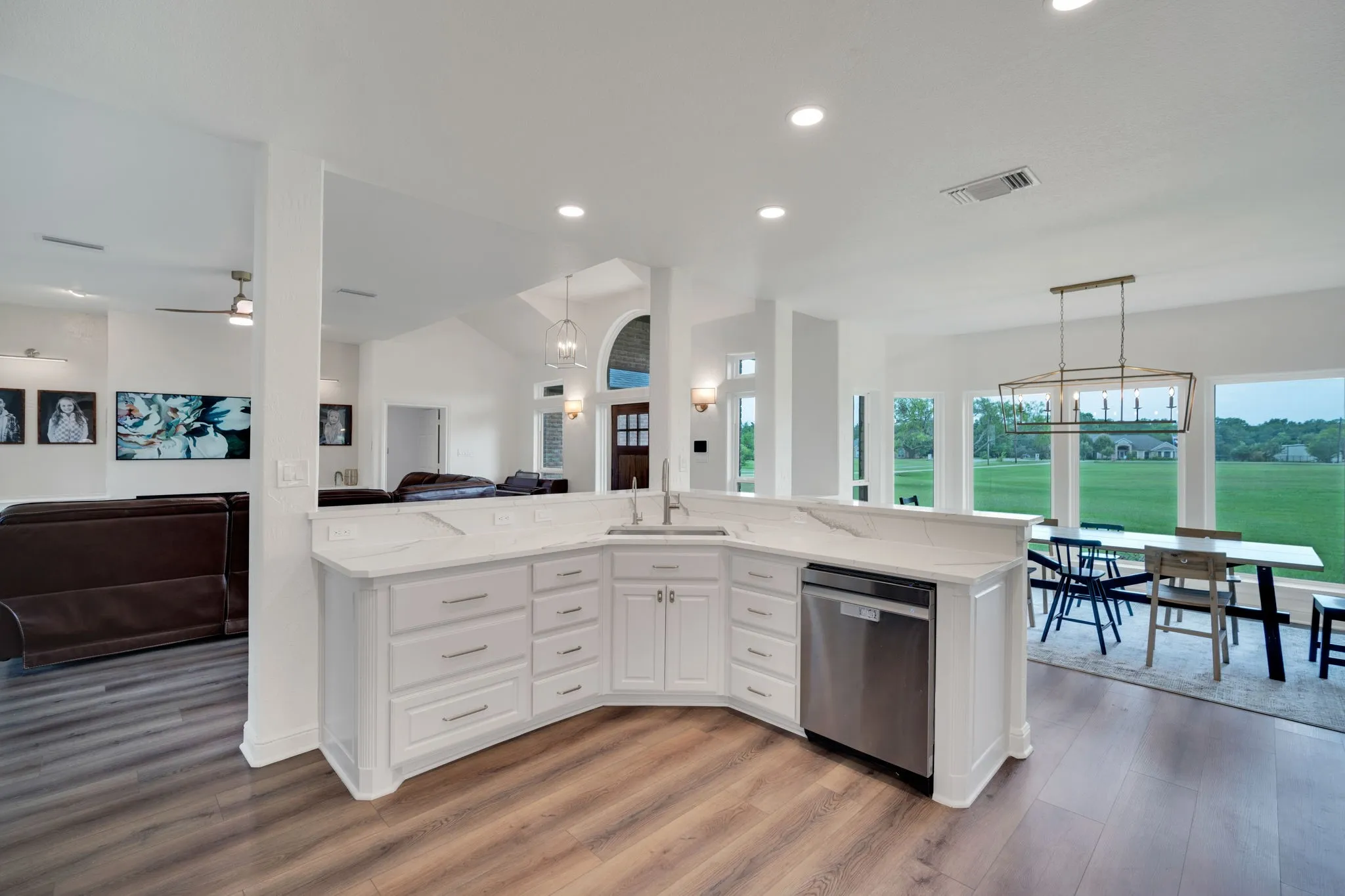 Curved kitchen island with white cabinetry and a light-toned countertop, stainless steel sink, and built-in dishwasher
