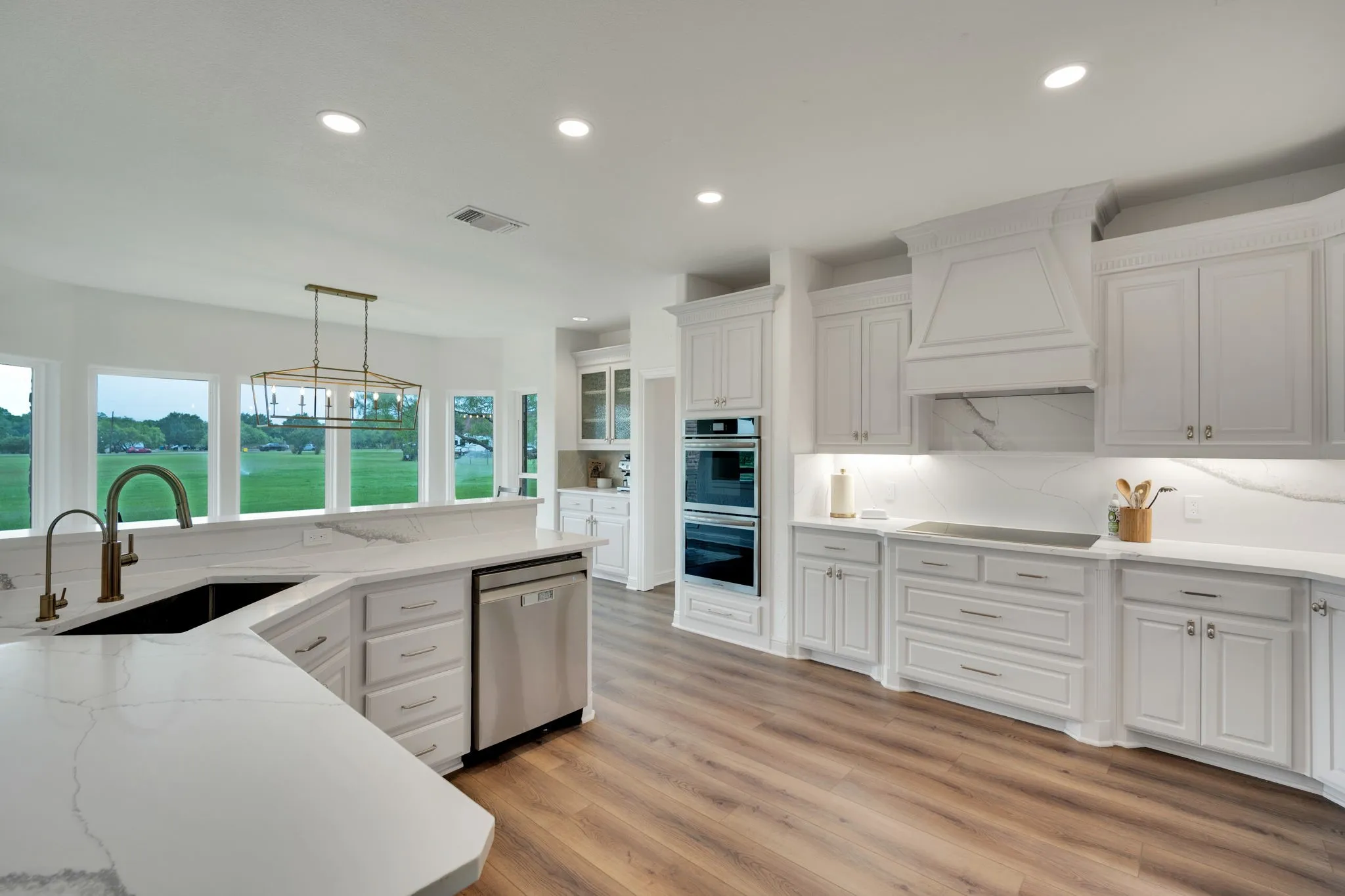 Open-concept kitchen featuring extensive cabinetry, quartz countertops with integrated backsplash, stainless steel double ovens, and under cabinet lighting.