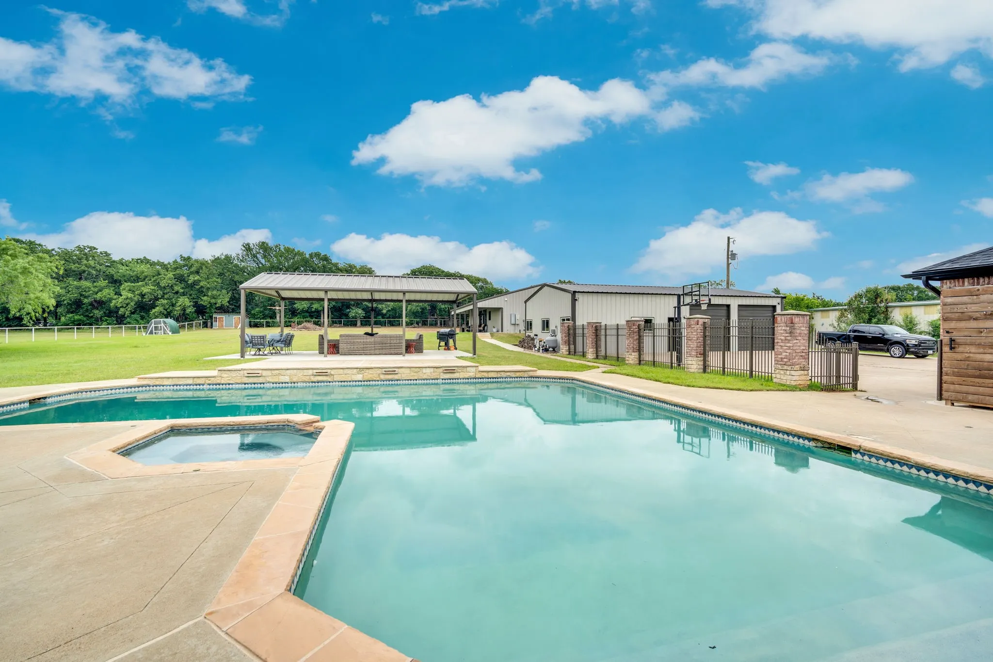 Outdoor area featuring a 45K gallon swimming pool with an integrated spa, a covered patio structure, and a large manicured lawn