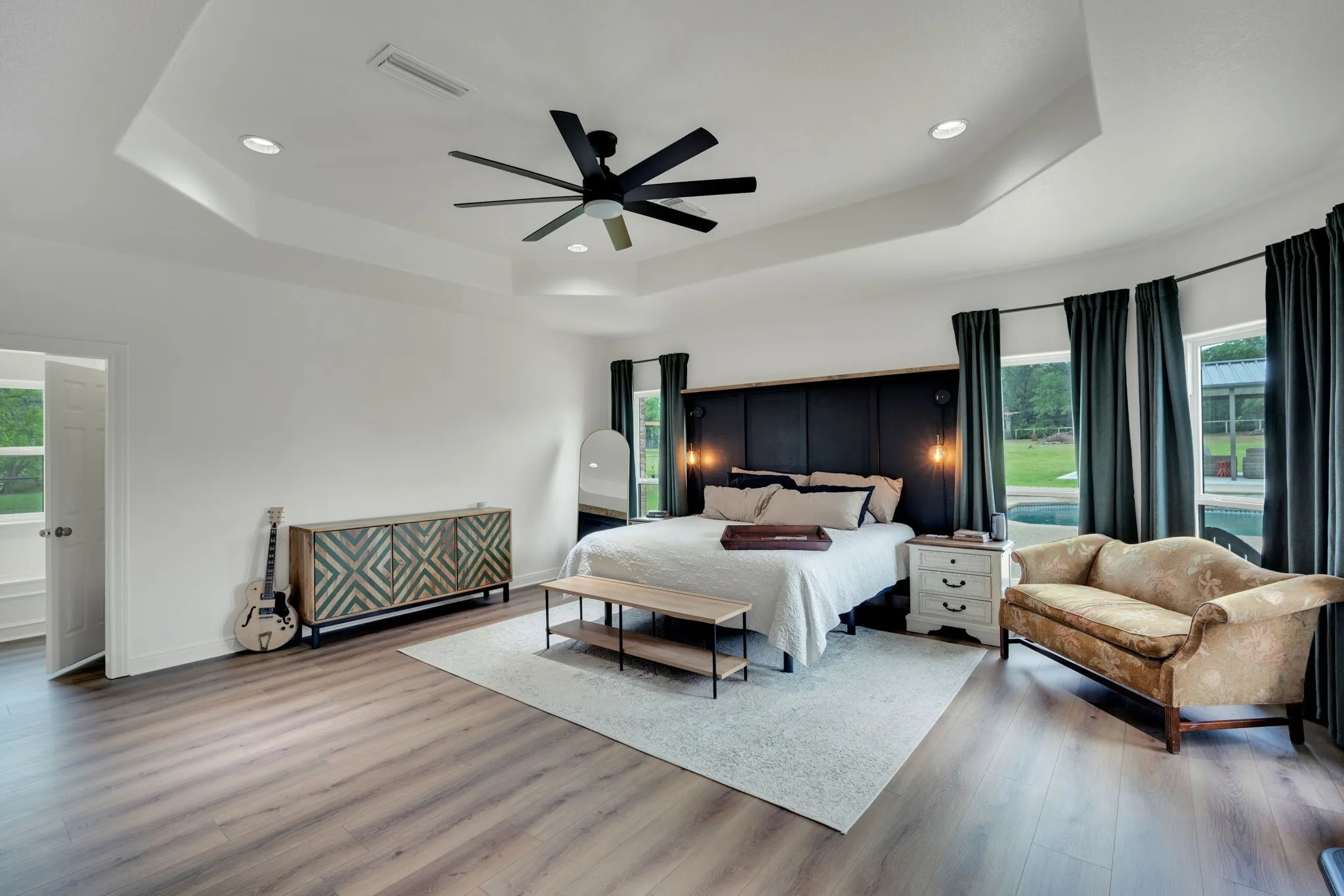 Spacious primary room featuring tray ceilings, recessed lighting, sitting area and multiple windows with outdoor pool​​‌​​​​‌​​‌‌​‌‌​​​‌‌​‌​‌​‌​​​‌​​ views