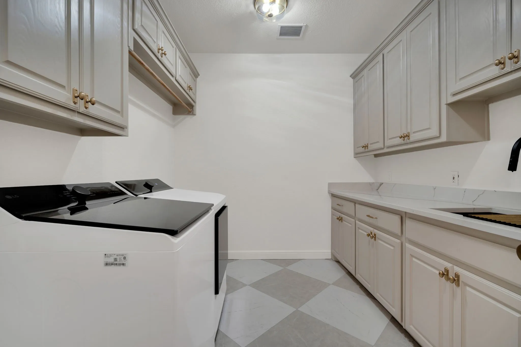 Laundry area featuring TWO washer and dryer hookups, a checkered tile floor, ample light cabinetry with champagne bronze hardware, a laundry sink, and a clothes hanging rod.