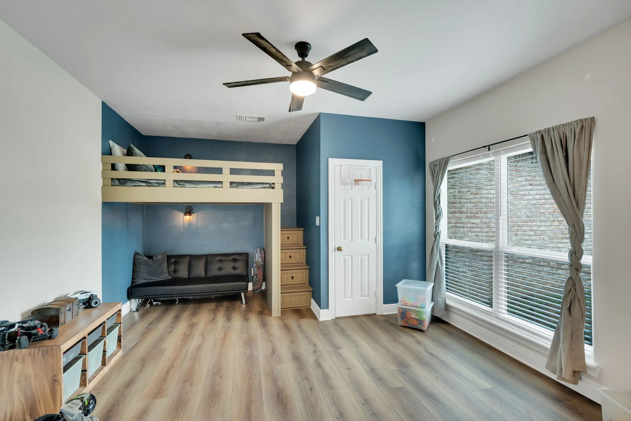 Bedroom 5 featuring a built-in loft bed with integrated storage steps, space blow the bed for a sitting area of another bed, a ceiling fan, walk-in closet, and a multi-pane window with a view of the side yard.