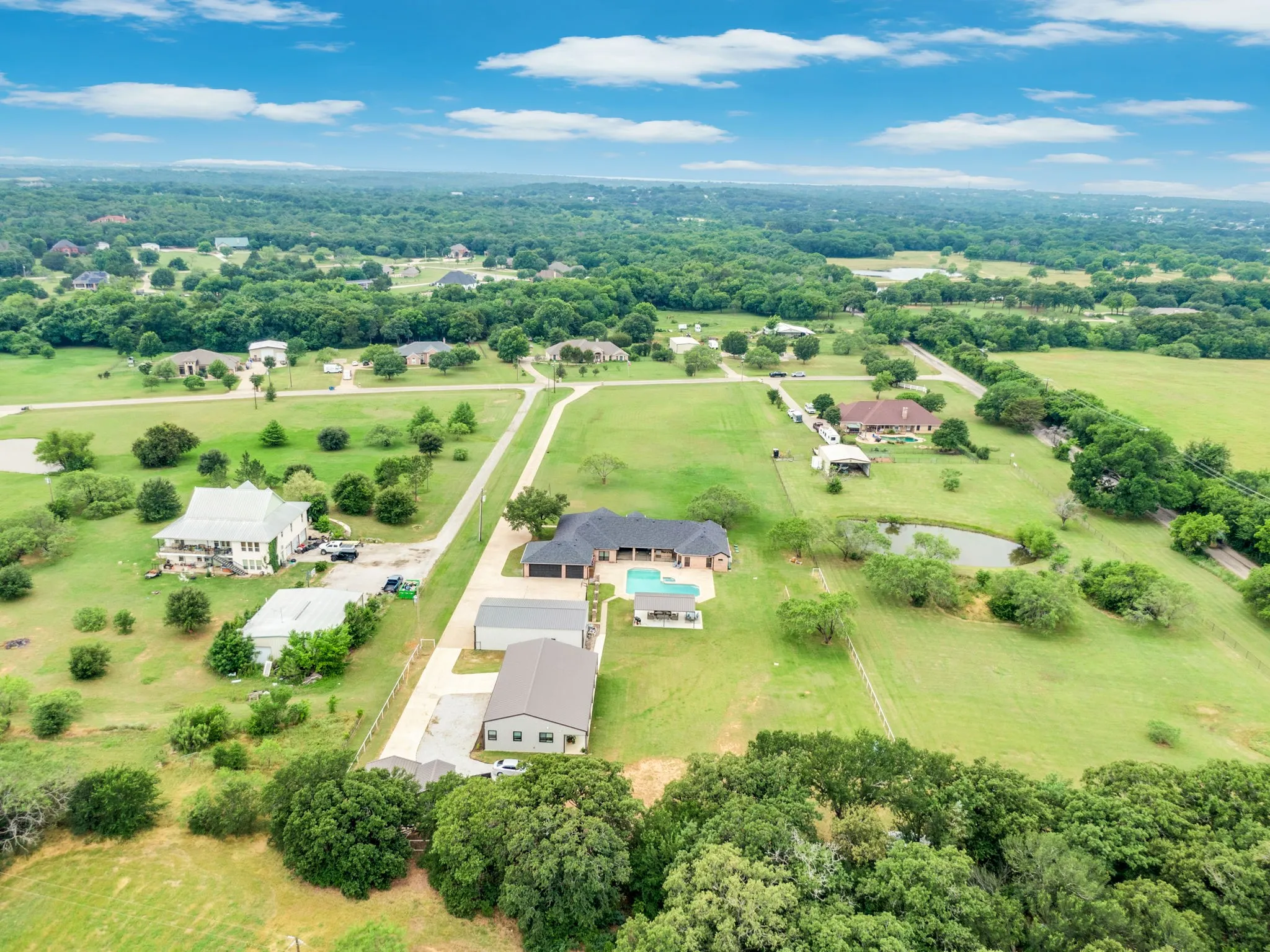 Expansive property featuring a swimming pool, detached garage, and a private pond amidst green fields and mature trees