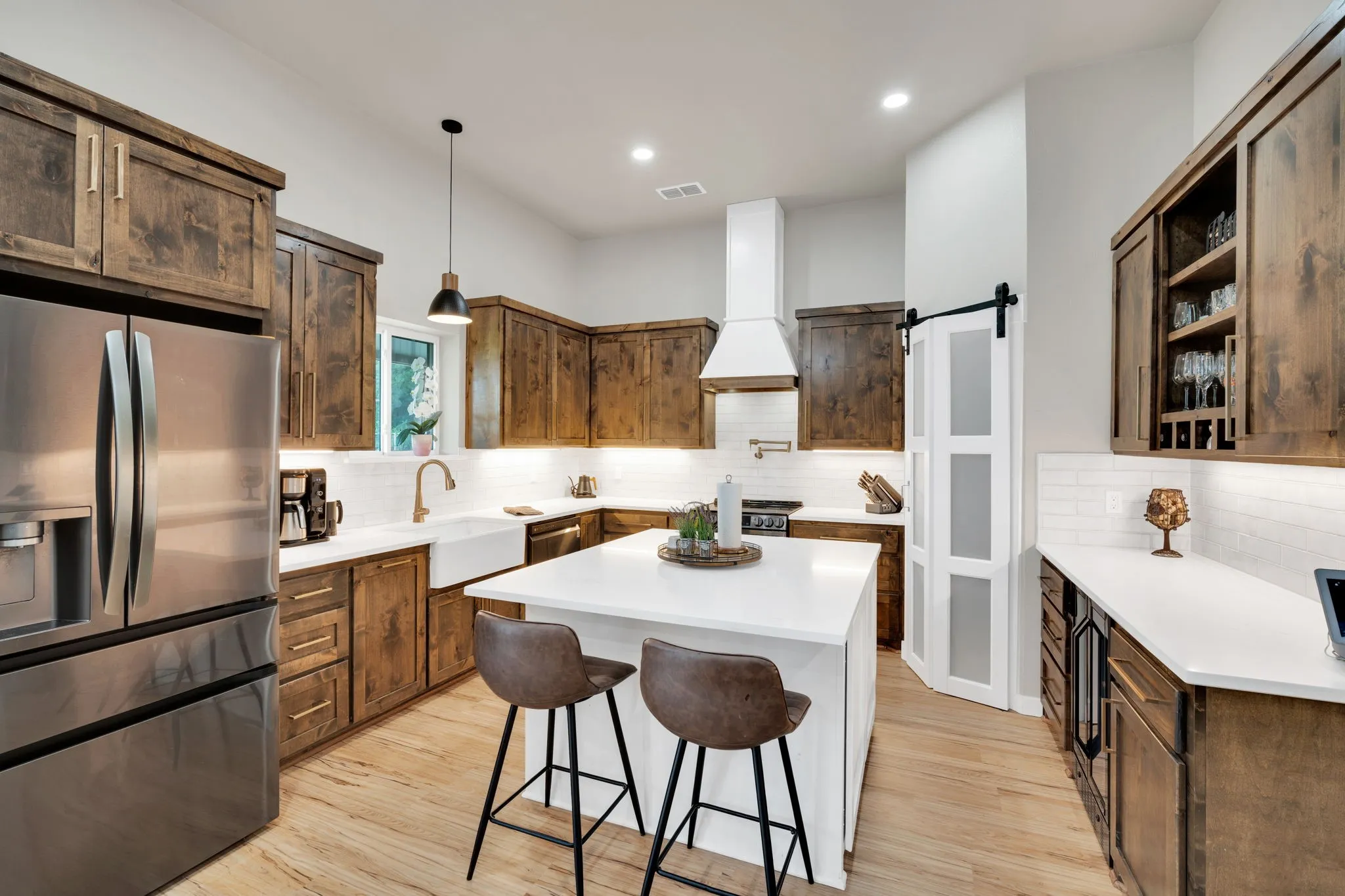 Gourmet kitchen featuring a central island with countertop seating, stainless steel appliances, a farmhouse sink, subway tile backsplash, quartz countertops, and wood-finish flooring