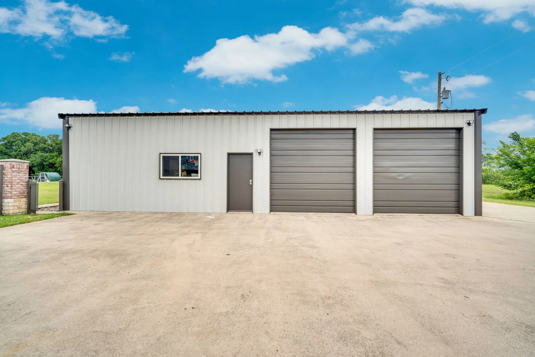 Metal-sided structure featuring two roll-up garage doors, a pedestrian entry door, and a single window. This shop holds an office space with a conference area and four offices.