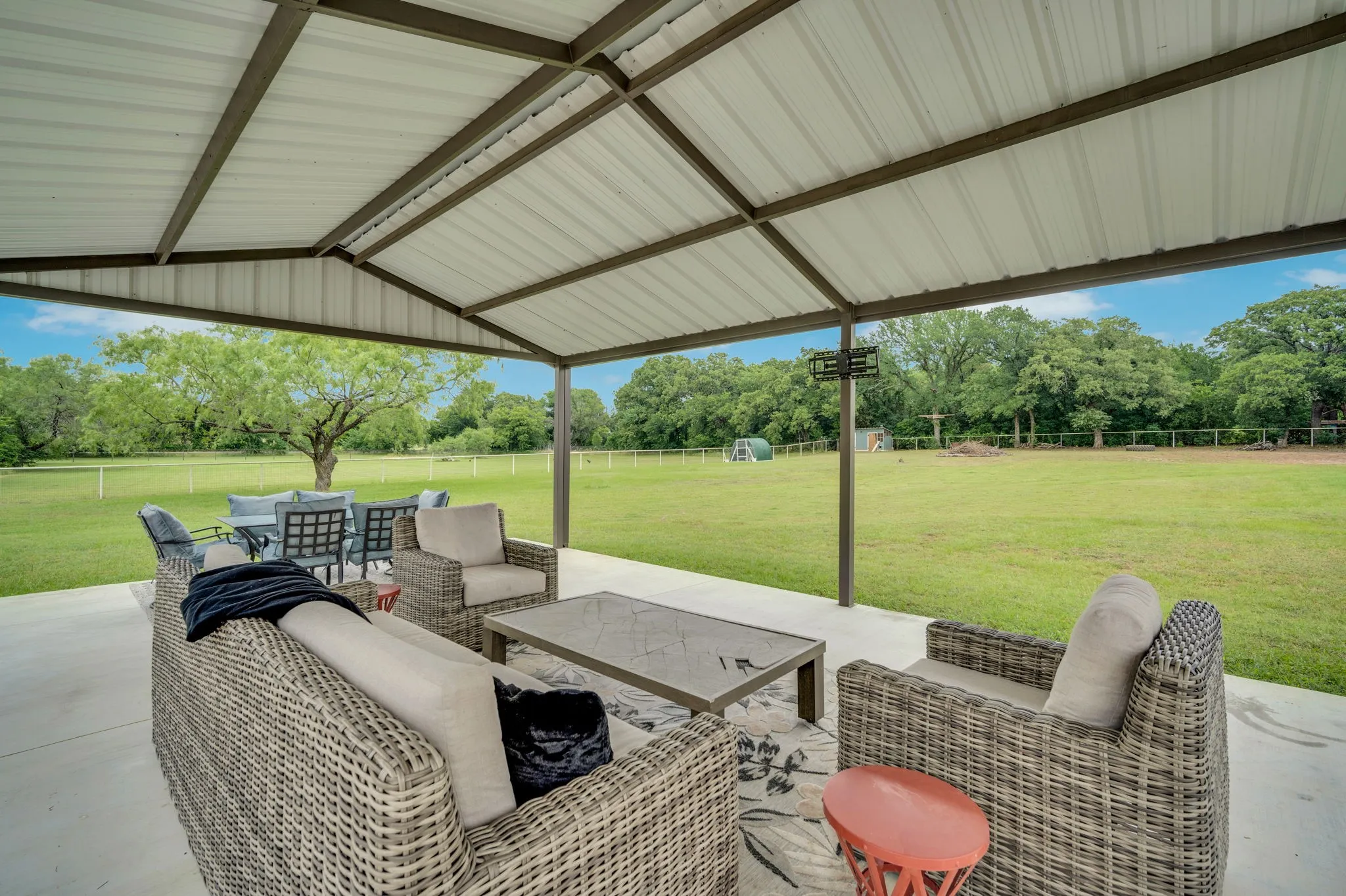 Expansive covered patio with a metal roof and concrete flooring - this concrete slab has an over hang and footers to add a large outdoor fireplace. This patio is ready for some serious upgrades. To the left of the patio is a permeant 4 person swing set.