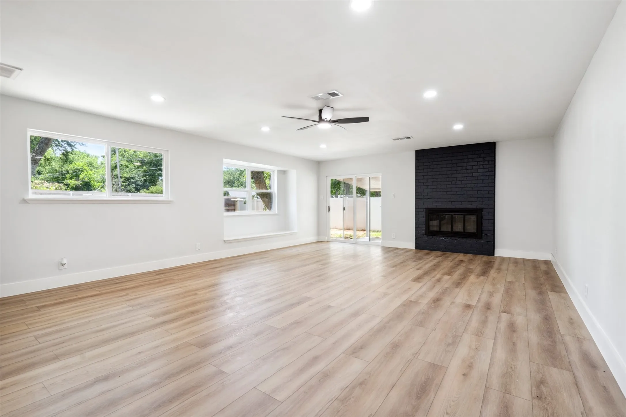 Spacious interior with wood-finish flooring, a contemporary black brick fireplace, recessed lighting, and a ceiling fan