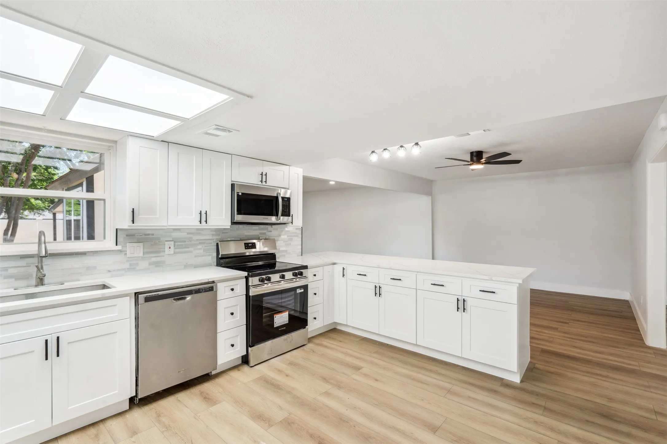 Modern kitchen featuring white shaker cabinetry, stainless steel appliances, light-toned wood-finish flooring, and a stone-finish countertop with a breakfast bar