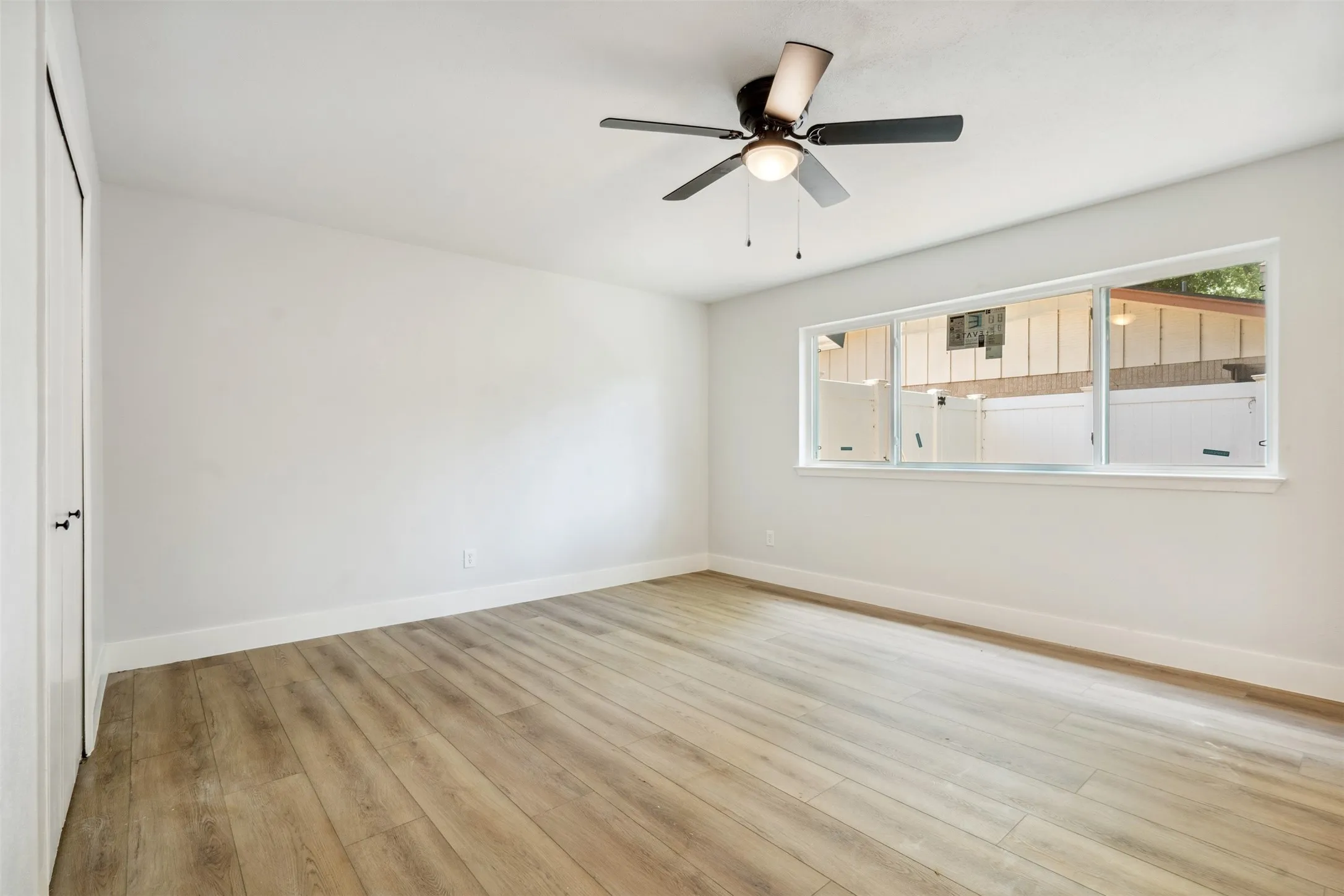 Spacious room featuring wood-finish flooring, crisp white walls, and a multi-pane window