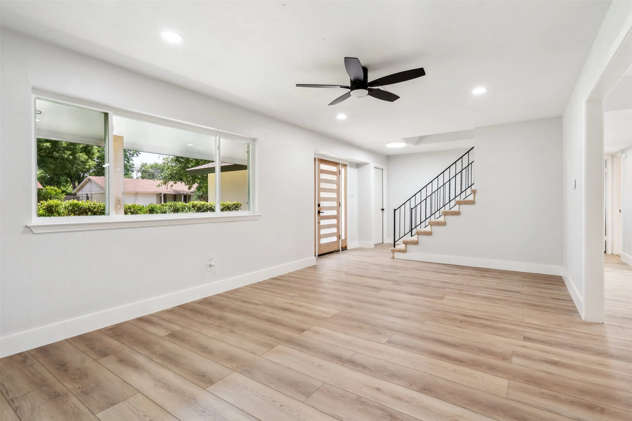 Spacious open area featuring light wood-finish flooring, a contemporary ceiling fan, and recessed lighting