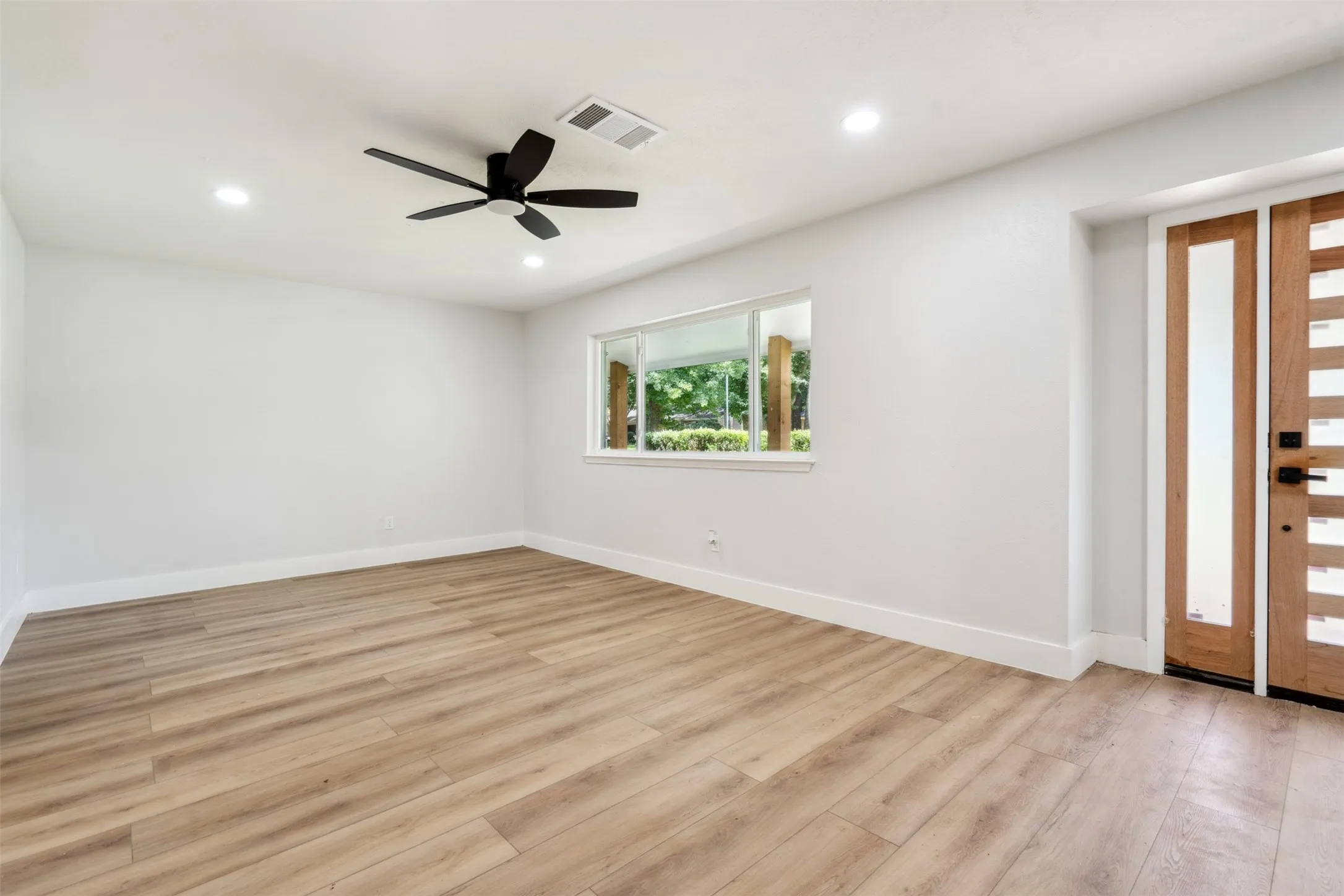 Spacious room with wood-finish flooring, white walls, and recessed lighting