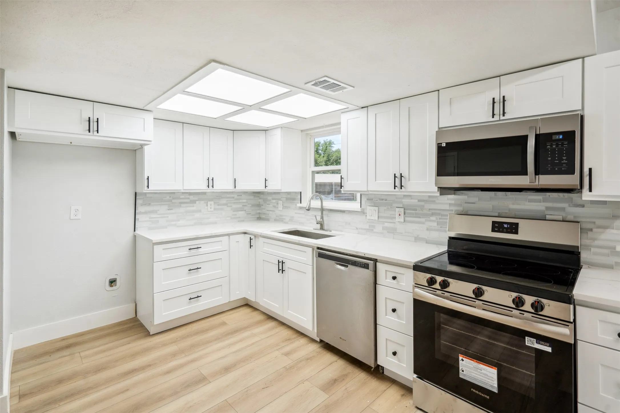 Bright kitchen featuring white shaker cabinetry with dark hardware, stone countertops, and a full tile backsplash