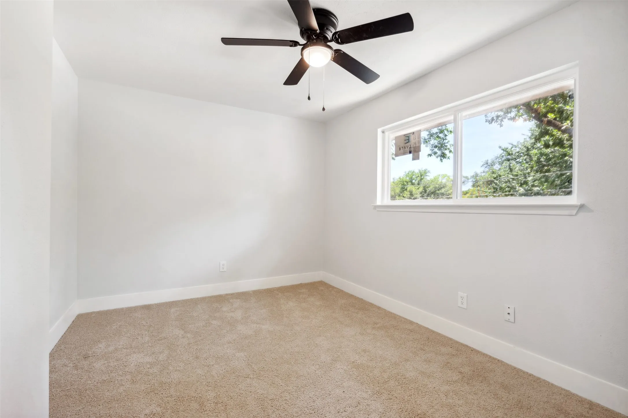 Carpeted room featuring a white window frame, white walls, white baseboards, and a dark-toned ceiling fan with integrated lighting