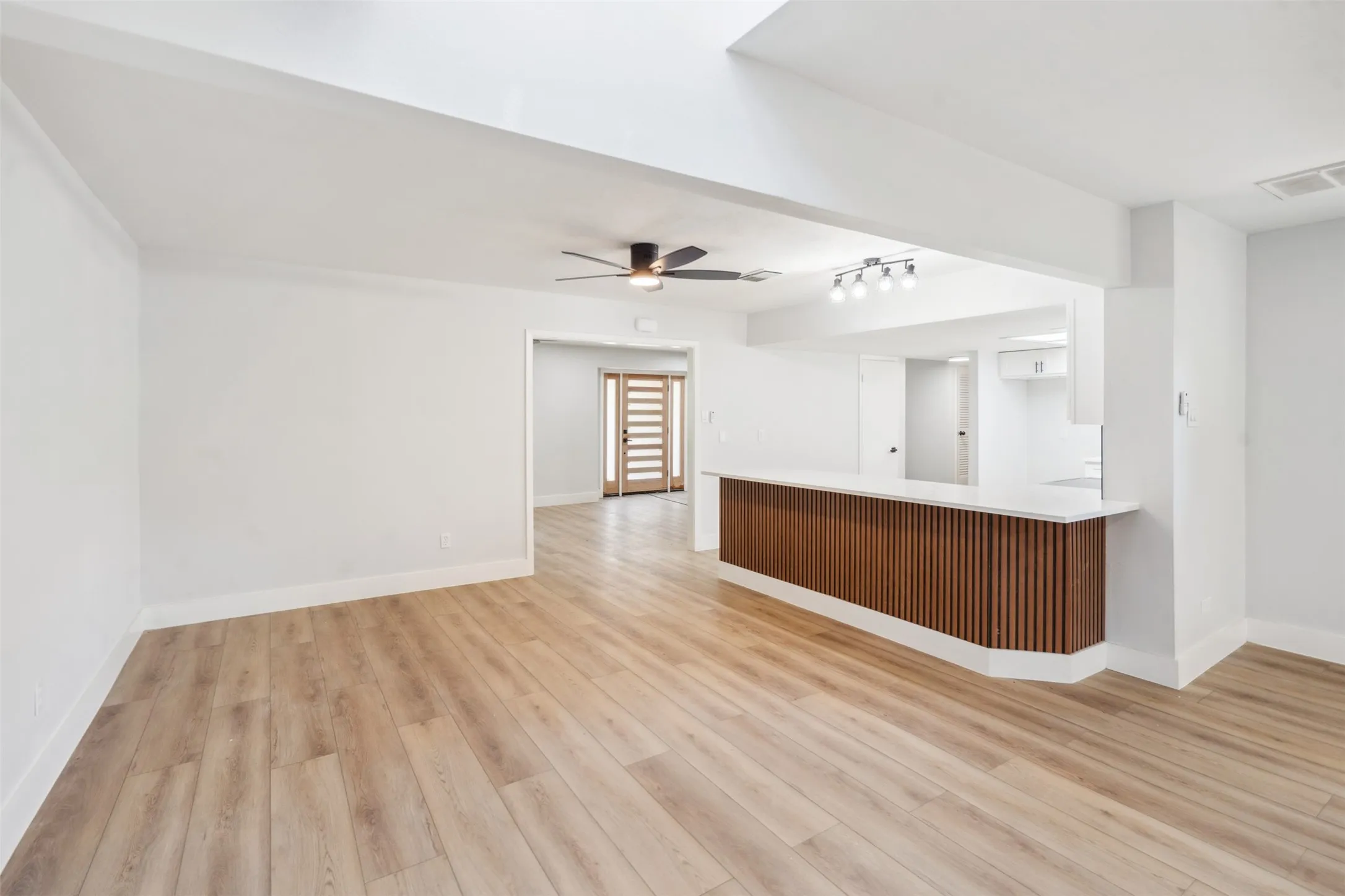 Open-concept living space featuring wood-finish flooring, a contemporary ceiling fan, and a wood-slat breakfast bar with a white countertop
