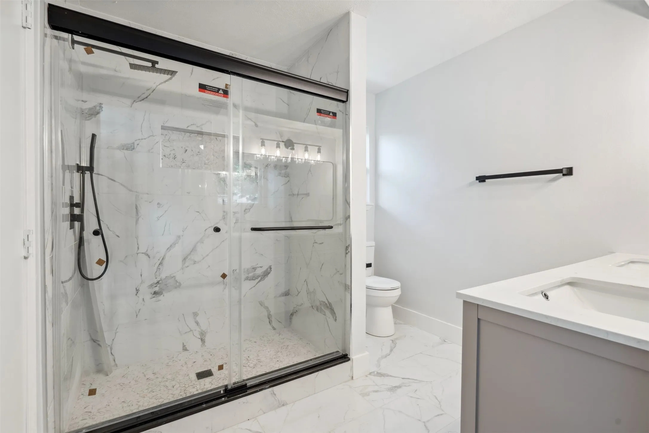 Contemporary bathroom featuring a spacious shower with black-framed glass doors, marble-patterned tile, and a matte black shower system