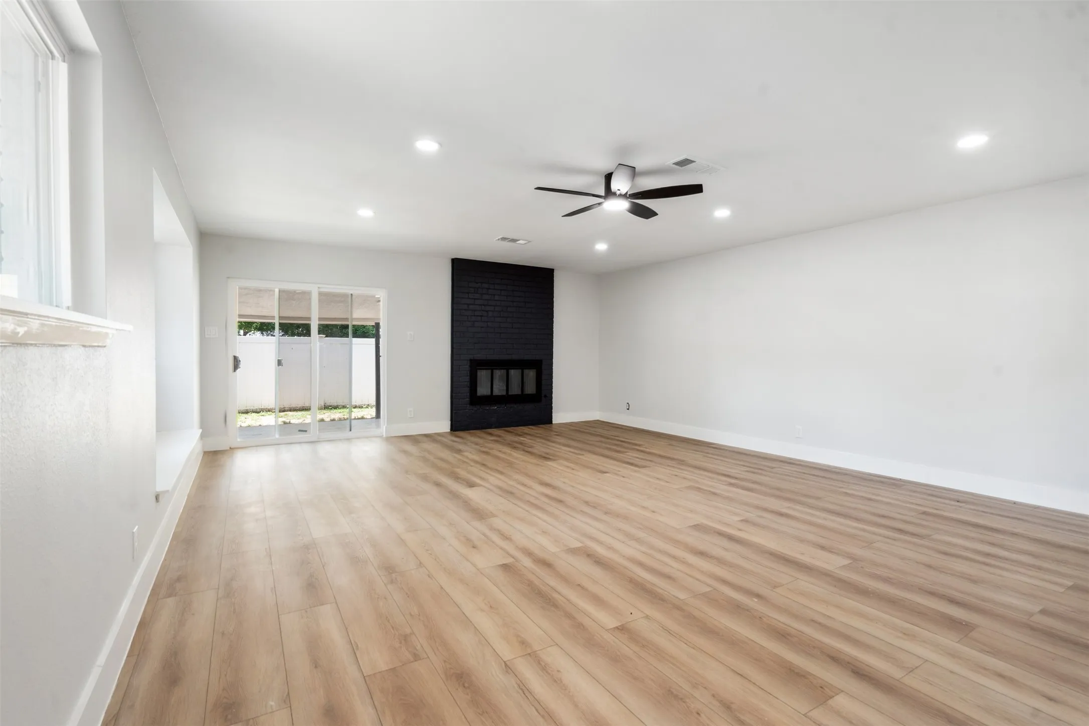 Spacious room featuring wood-finish flooring, a black brick fireplace, recessed lighting, and a ceiling fan