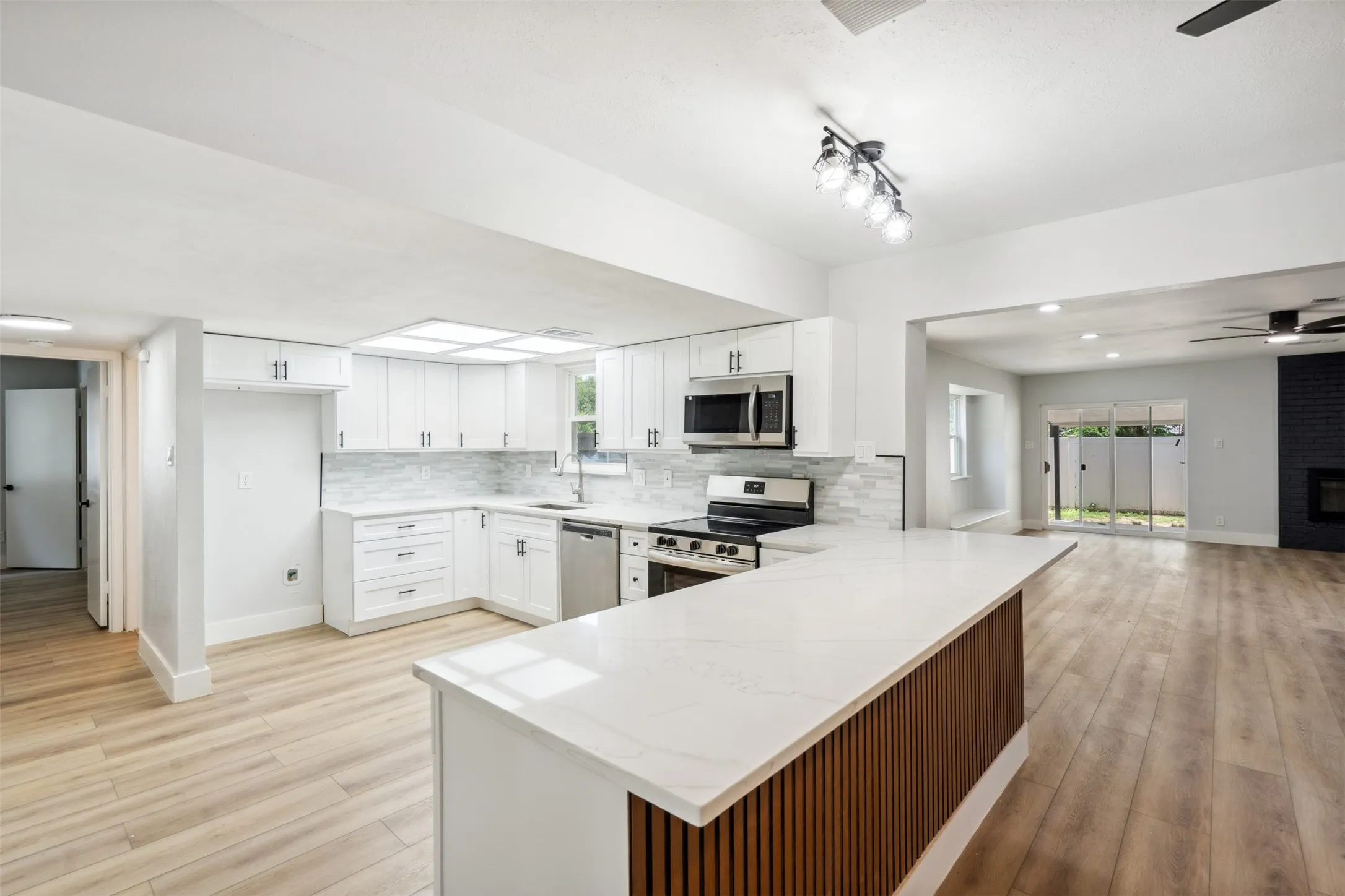 Modern kitchen featuring white cabinetry with dark hardware, stainless steel appliances, a white tile backsplash, and light wood-finish flooring