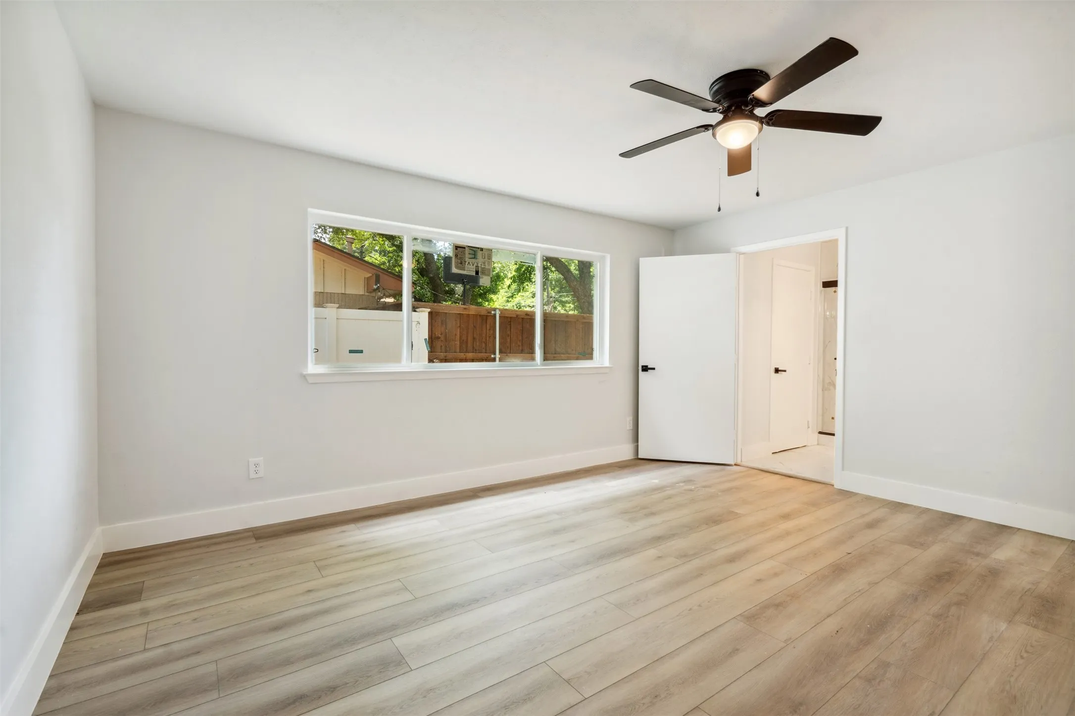 Spacious interior featuring wood-finish flooring, a large window, white trim, and a ceiling fan with integrated lighting