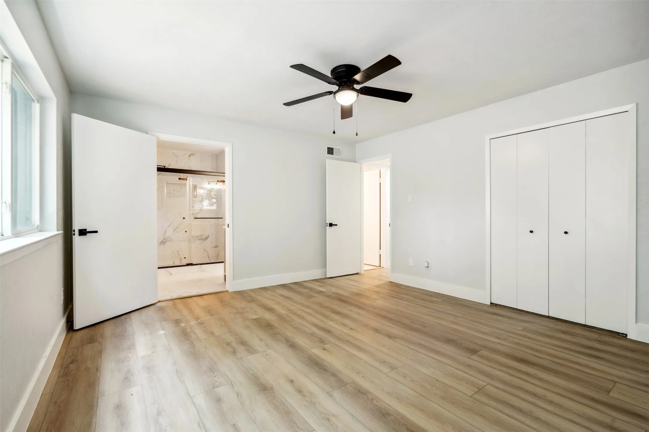 Spacious room featuring wood-finish flooring, light-toned walls, and a modern ceiling​​‌​​​​‌​​‌‌​‌‌​​​‌‌​‌​‌​‌​​​‌​​ fan