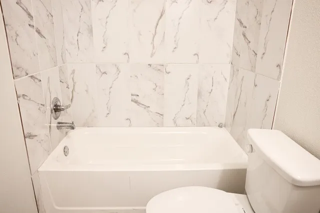 White porcelain bathtub with chrome fixtures and white tiled surround featuring gray veining