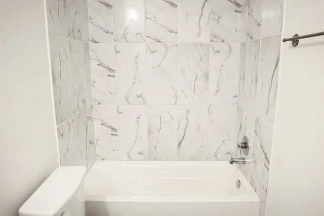 White bathtub with chrome fixtures and white marble-look wall tiling