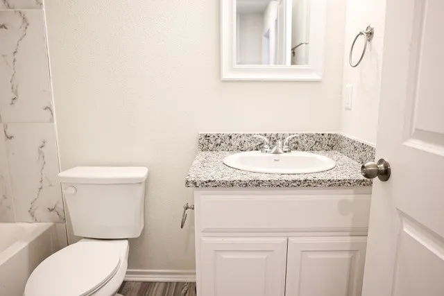 Full bathroom featuring a white toilet, coordinating vanity with a granite countertop, and an undermount sink