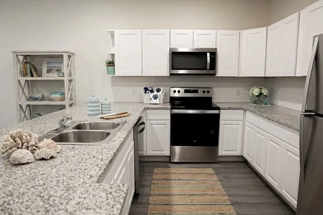 Kitchen featuring granite countertops, white cabinetry, a double basin sink, stainless steel appliances, and wood-finish flooring